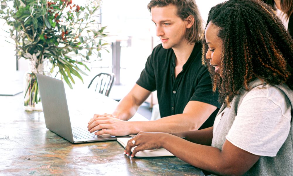 Man and woman are sitting at a desk looking at a computer together