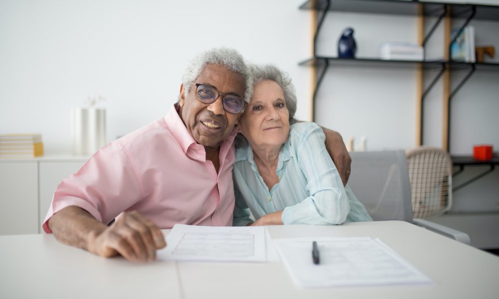 An elderly couple are hugging and looking into the camera lens