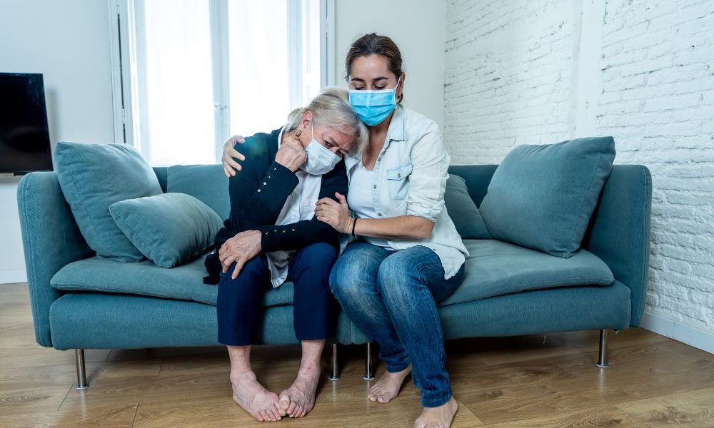 nursing home sexual assault. A younger woman in a mask comforts an older woman in a mask